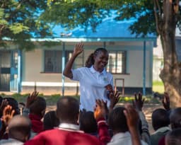 A facilitator and schoolchildren with raised hands during an outdoor session.