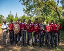Schoolchildren holding tree seedlings under trees.