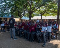 A facilitator leading a school session, children raising their hands.